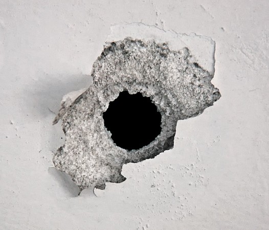Mottoplakat: Schussloch in einer Wand